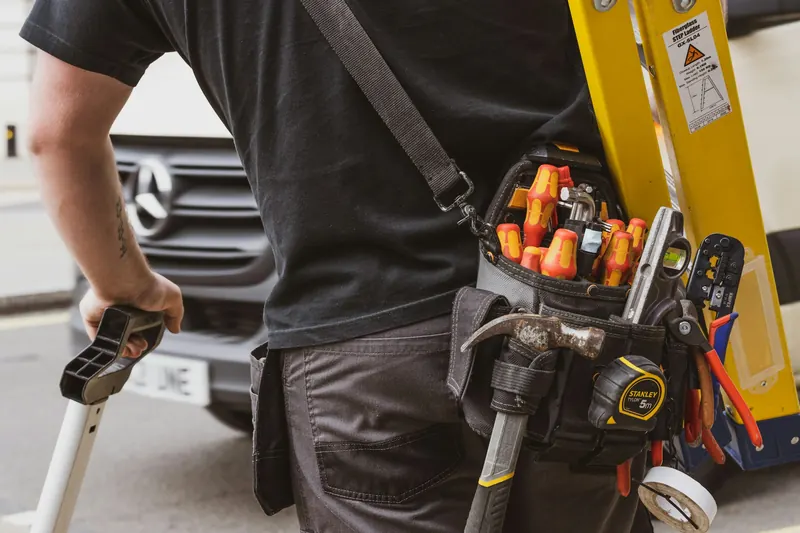 Un installateur, sa ceinture d'outils, devant sa camionnette